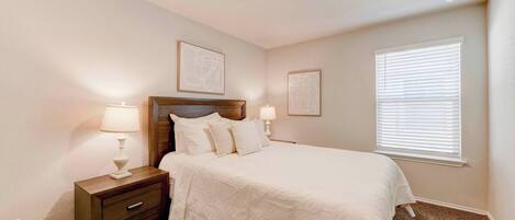 A bedroom with a bed, nightstands, wall art, and a window with blinds.
