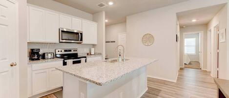 A modern kitchen with white cabinetry, a granite countertop, and a built-in microwave.