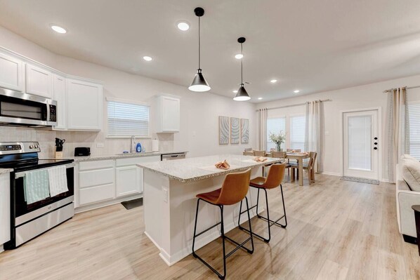 A modern kitchen with white cabinetry, a central island, bar stools, and pendant lighting. - Spacious 4 Bedroom House in Temple with 5 Beds (Temple)