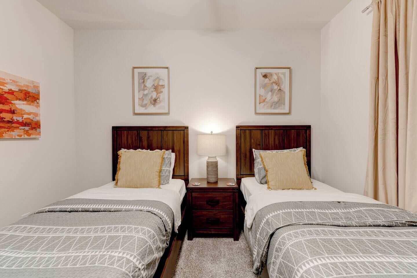 A double room with two beds, a nightstand with a lamp, and artwork on the walls.
