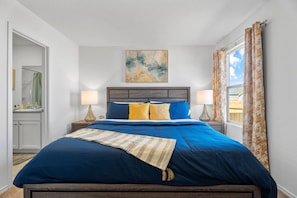 A bedroom with a bed, two bedside lamps, a painting, and a window with curtains. - Business Haven in New Braunfels with 5 Beds (New Braunfels)
