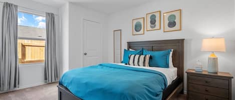 Un dormitorio con una cama, una mesita de noche, una lámpara y una ventana con cortinas.
