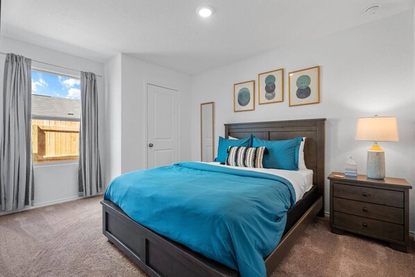 Un dormitorio con una cama, una mesita de noche, una lámpara y una ventana con cortinas.