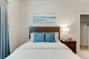 Une chambre d’hôtel avec un lit, une table de chevet, une lampe, un tableau représentant une plage et une armoire.