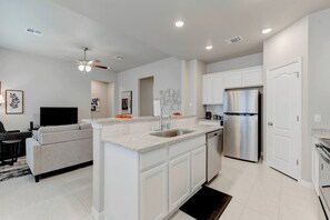 A modern kitchen with white cabinetry, a stainless steel refrigerator, and a built-in island with a sink.
