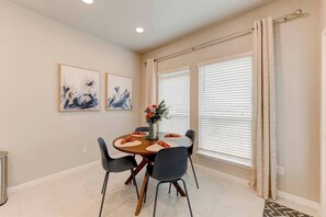 Un comedor con una mesa redonda, sillas, una obra de arte en la pared y una ventana con persianas.