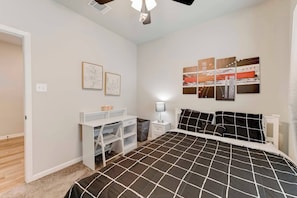 Quarto com cama, escrivaninha, cadeira, mesa de cabeceira e decoração na parede.
