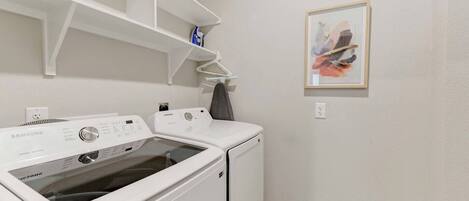 A laundry room with a Samsung washer and dryer, a shelf above the washer, and a framed picture on the wall.