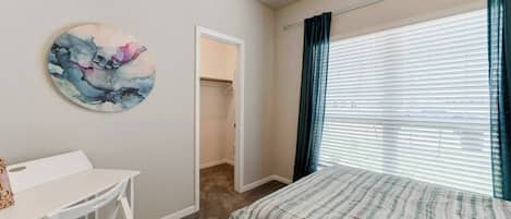 A bedroom with a bed, a desk, a chair, a closet, and a window with curtains.