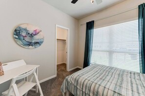 A bedroom with a bed, a desk, a chair, a closet, and a window with curtains.