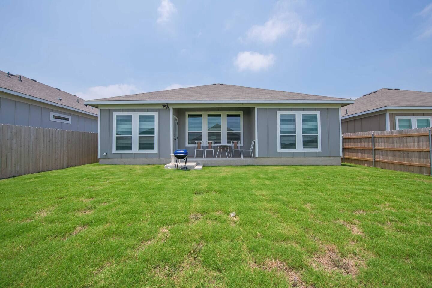 A residential house with a fenced backyard, a barbecue grill, and a patio with chairs.