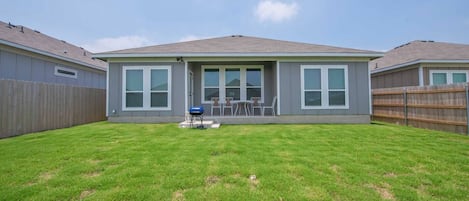 Une maison d’habitation avec un jardin clôturé, un barbecue et une terrasse avec des chaises.