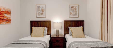 A double room with two beds, a nightstand, a lamp, and artwork on the walls.