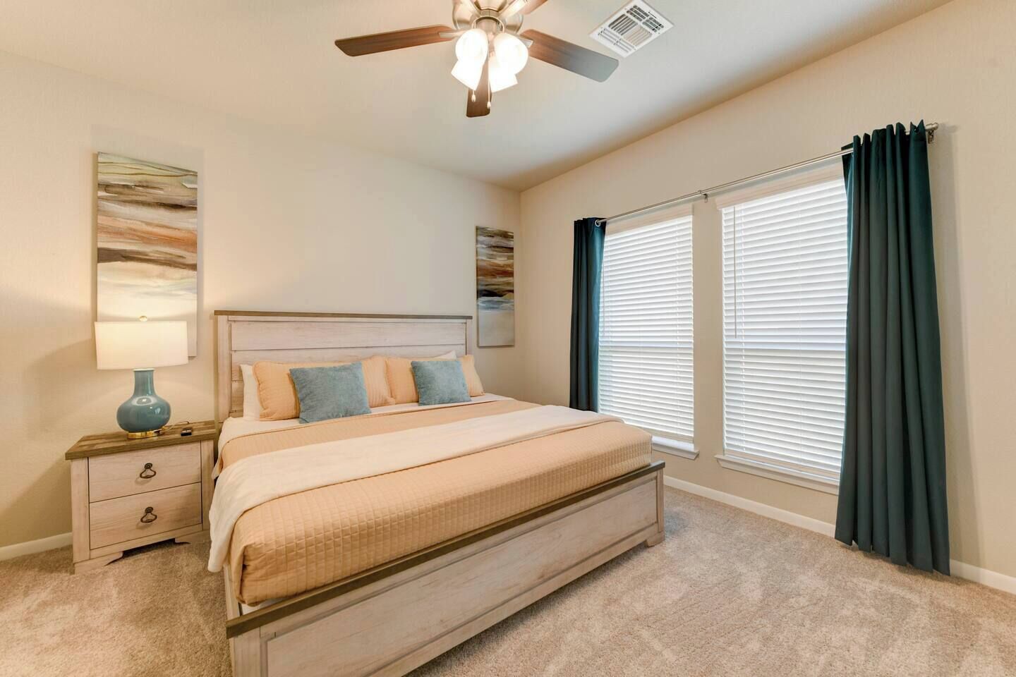 A bedroom with a bed, nightstand, lamp, ceiling fan, and large windows with curtains.