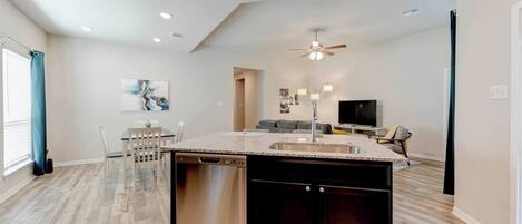 A modern kitchen with a central island, built-in dishwasher, and a ceiling fan.