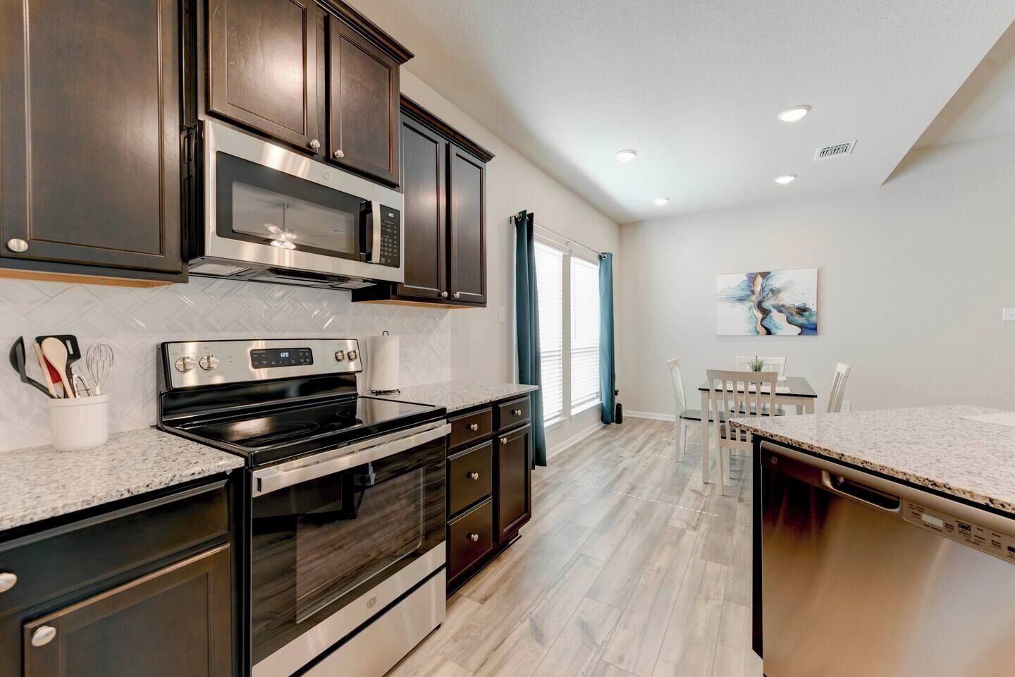 A modern kitchen with dark cabinetry, stainless steel appliances, and a dining area with a table and chairs.