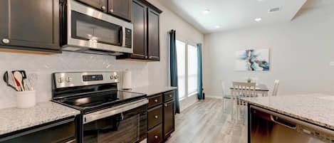 A modern kitchen with dark cabinetry, stainless steel appliances, and a dining area with a table and chairs.