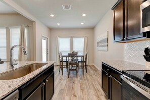 Una cocina moderna con encimeras de granito, electrodomésticos de acero inoxidable y un comedor con mesa y sillas.