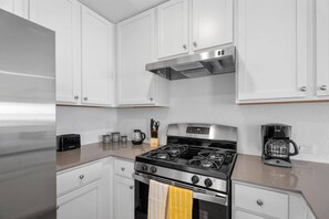 A modern kitchen with white cabinetry, a stainless steel refrigerator, a gas stove, and a coffee maker. - Modern Comfort in New braunfels (New Braunfels)