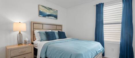 A bedroom with a bed, nightstand, lamp, and a painting on the wall.
