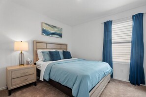A bedroom with a bed, nightstand, lamp, and a painting on the wall.
