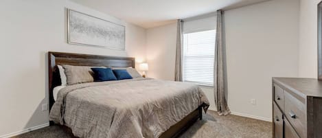 A bedroom with a bed, a nightstand, a dresser, a ceiling light, and a window with curtains.
