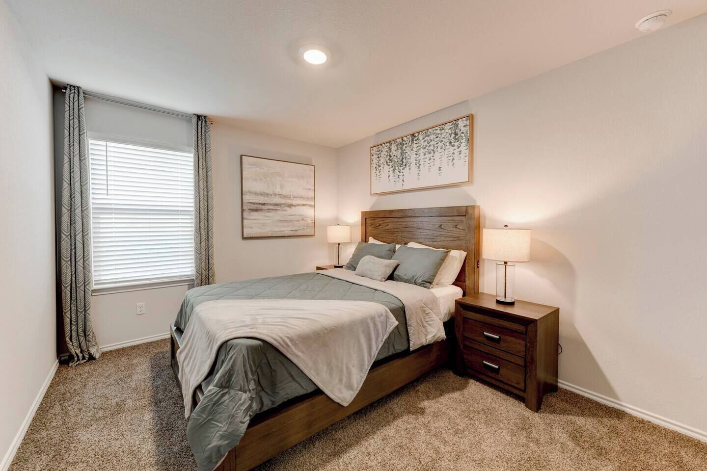 A bedroom with a bed, bedside tables, a window with curtains, and wall art.