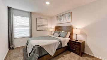 A bedroom with a bed, bedside tables, a window with curtains, and wall art.