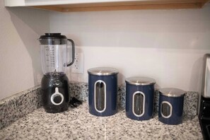 A kitchen counter with a blender, three blue containers, and a microwave.