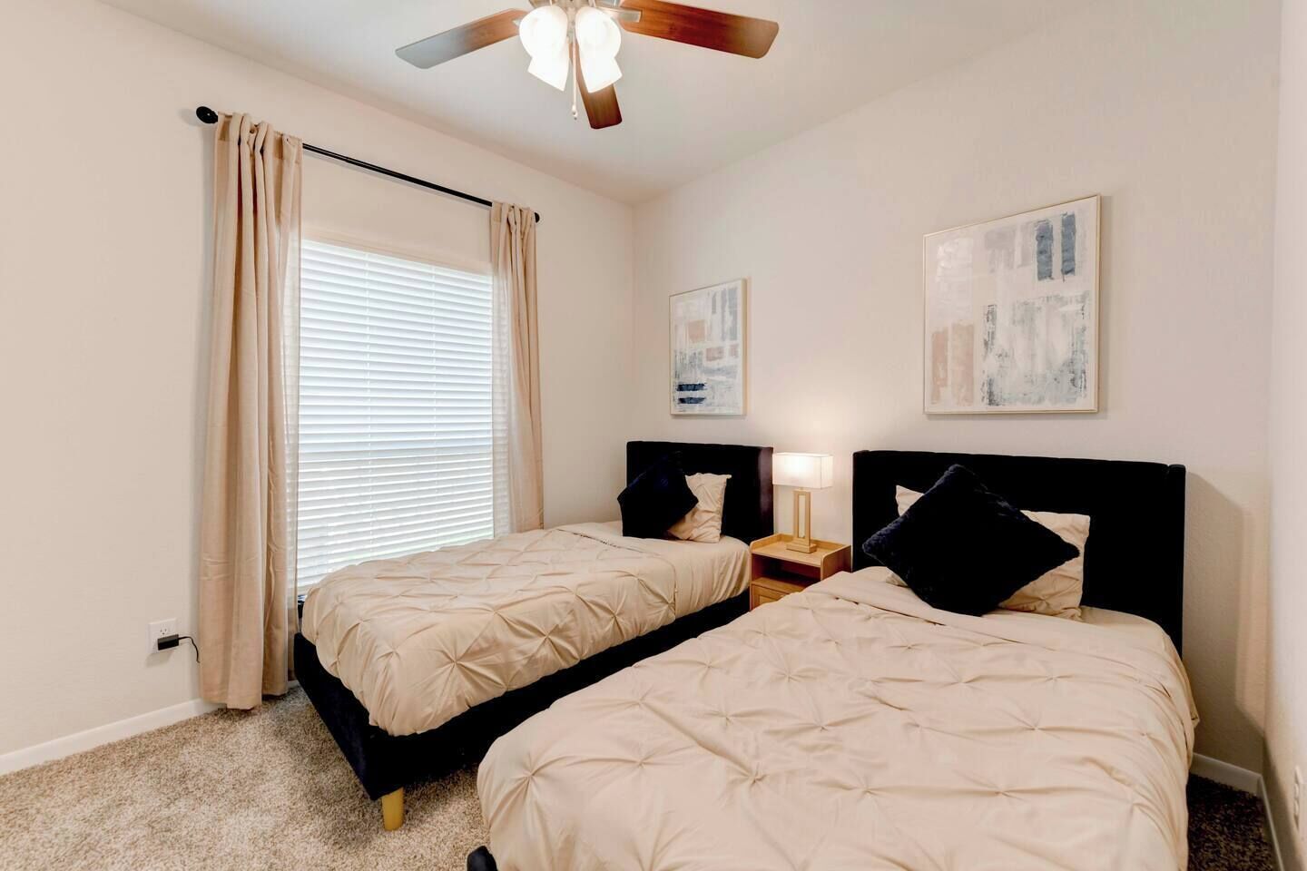 A bedroom with two beds, a ceiling fan, and artwork on the walls.