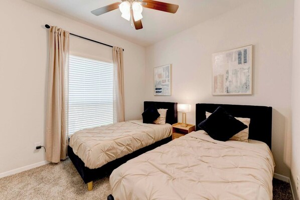 A bedroom with two beds, a ceiling fan, and artwork on the walls.