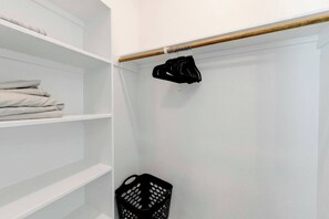 A white closet with shelves, a wooden rod, and a black garment hanging.