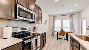 A modern kitchen with stainless steel appliances, wooden cabinets, a dining area with a table and chairs, and a window with curtains. - Spacious Modern 5 beds House in Troy (Troy)