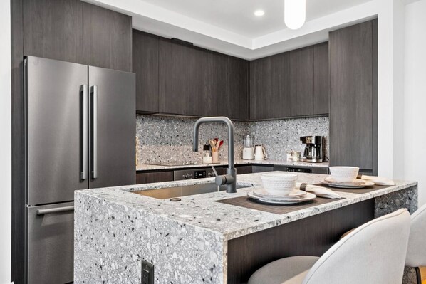 Una cocina moderna con armarios de madera oscura, encimera de granito, electrodomésticos de acero inoxidable y una isla integrada con asientos.
