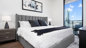 Ein modernes Schlafzimmer mit einem großen Bett, zwei Nachttischen, Blick auf die Stadt und einem gerahmten abstrakten Gemälde.