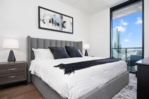 Ein modernes Schlafzimmer mit einem großen Bett, zwei Nachttischen, Blick auf die Stadt und einem gerahmten abstrakten Gemälde.