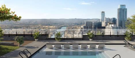 A rooftop pool with a city view, potted plants, and a glass railing.