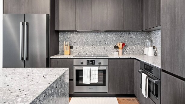 Eine moderne Küche mit dunklen Holzschränken, einem Edelstahl-Kühlschrank, einem Bosch-Backofen und einer Arbeitsplatte aus Granit.