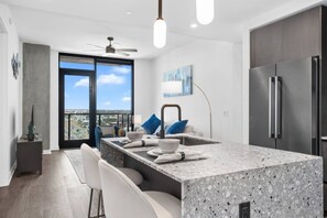 A modern kitchen with a large island, a refrigerator, and a view of the city.