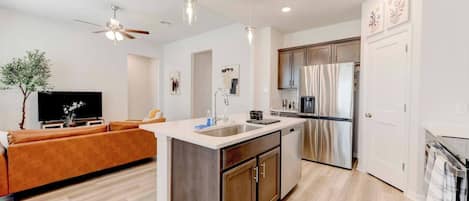 A modern kitchen with a central island, stainless steel appliances, and a dining area with a sofa.
