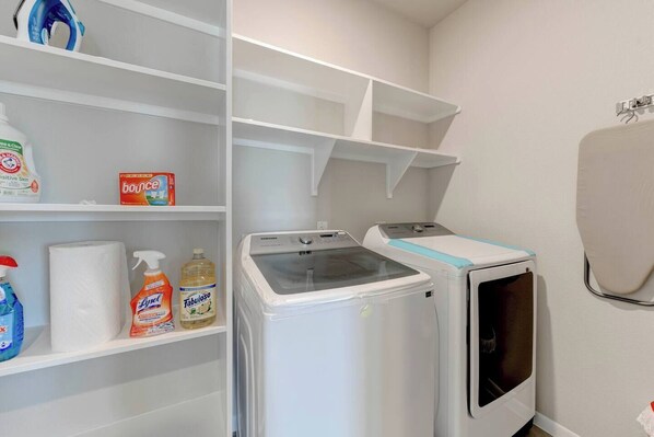Un espace buanderie comprenant un lave-linge, un sèche-linge, des étagères avec des produits de nettoyage et un porte-serviettes fixé au mur.