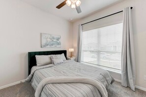 A bedroom with a bed, a nightstand, a lamp, a ceiling fan, and a window with blinds. - Dup Retreat in Troy with 5 Beds (Troy)