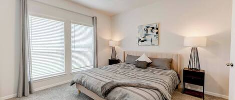 A bedroom with a bed, two bedside tables, a ceiling fan, and a window with blinds.