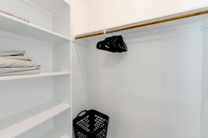 Un placard blanc avec des étagères, une tringle en bois et un vêtement noir suspendu.
