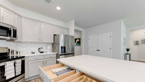 A modern kitchen with white cabinetry, stainless steel appliances, and a large wooden drawer organizer.