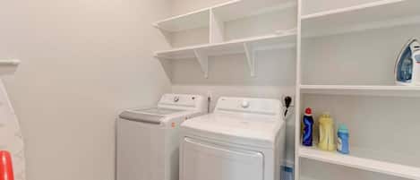 A laundry room with two washing machines, a drying machine, and shelves with cleaning supplies.
