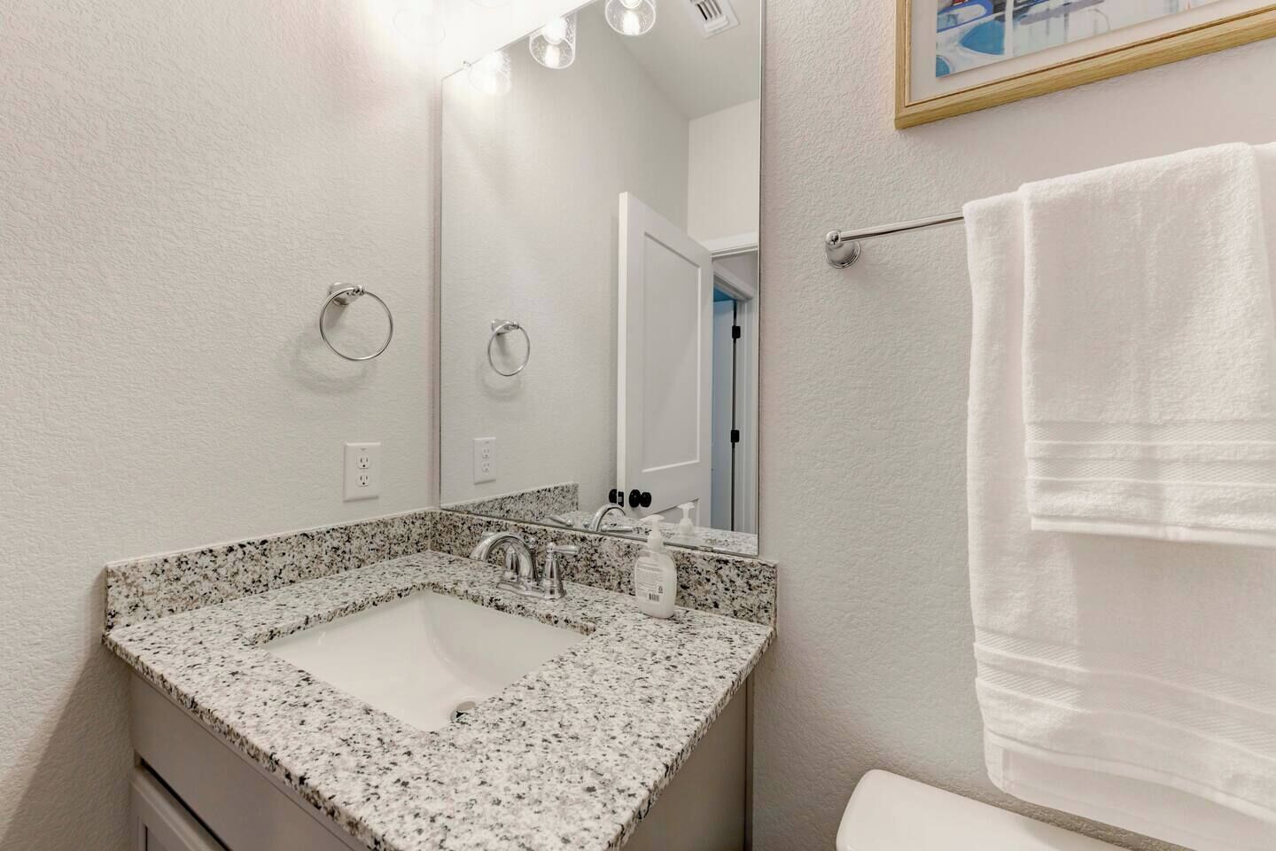 A bathroom with a granite countertop sink, a mirror, a towel rack, and a door leading to another room.