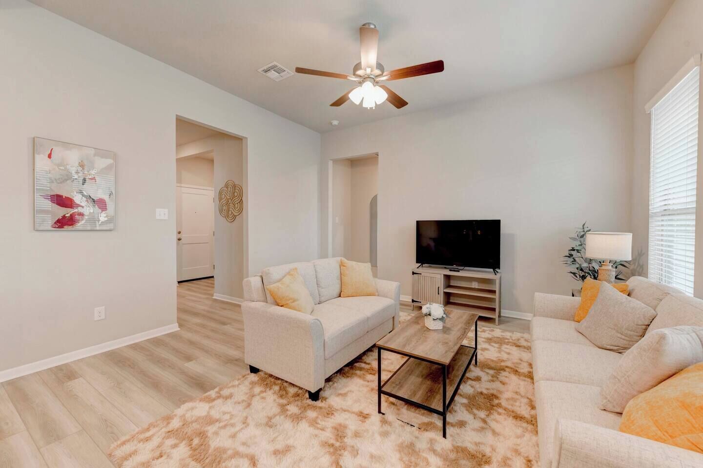 Un salon moderne doté d’un ventilateur de plafond, d’un téléviseur à écran plat et de deux canapés.
