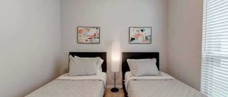 A small, clean room with two beds, a standing lamp, and abstract art on the walls.