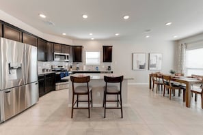 A modern kitchen with stainless steel appliances, a central island with bar stools, and a dining area with wooden chairs. - 4 Bedroom 3 Bath Home in Temple (Temple)